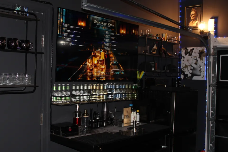 A modern bar with a large screen displaying a cocktail menu and bottles arranged on shelves.