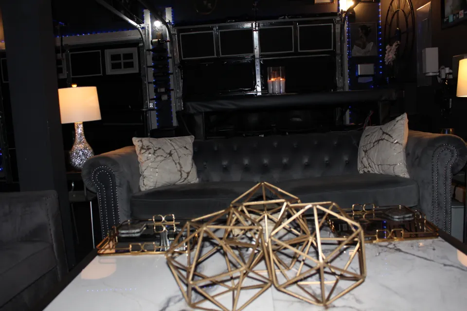 A deep gray velvet sofa with decorative pillows, in front of a coffee table adorned with geometric gold candlesticks.